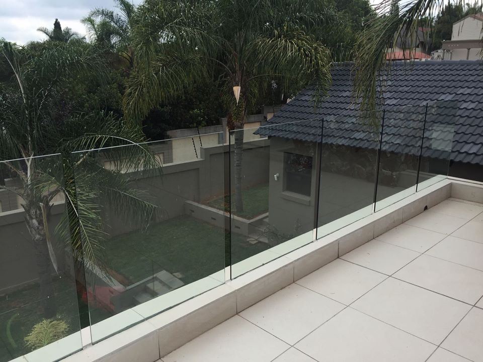Frameless glass balustrade on a rooftop terrace surrounded by palm trees